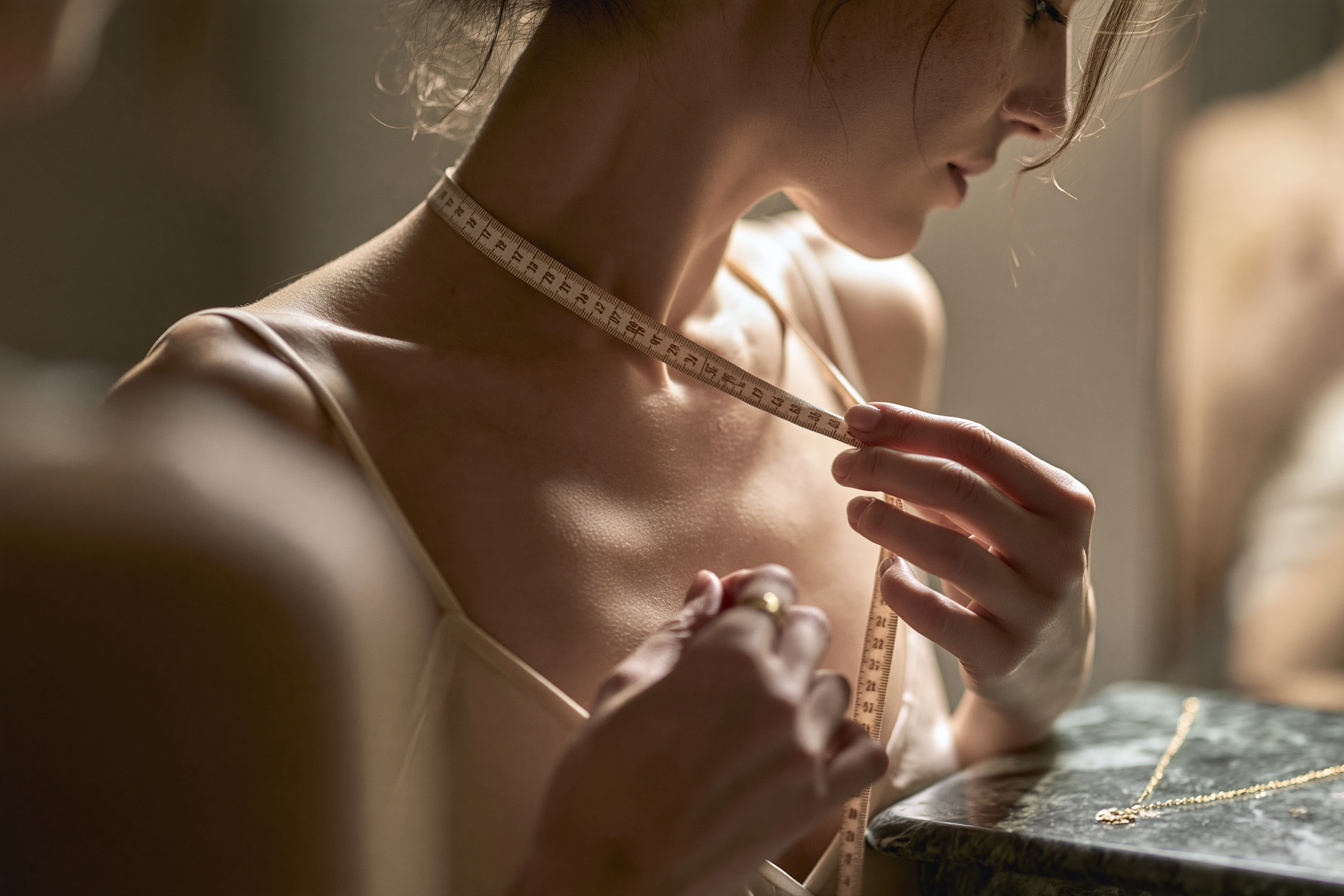 Woman measuring the desired necklace length with a soft tape measure at home